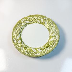 Puede incluir: Plato decorativo redondo, blanco y verde, con borde festoneado. El plato presenta un centro blanco y un borde verde con un diseño floral blanco. El plato mide unos 20 cm de diámetro y probablemente sea de cerámica o porcelana.