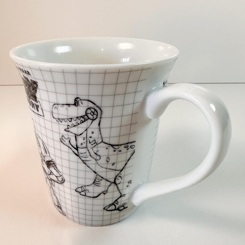 May include: White ceramic mug with a black and white cartoon dinosaur design. The mug has a grid pattern and a curved handle. A collectible item, the mug is suitable for hot beverages.
