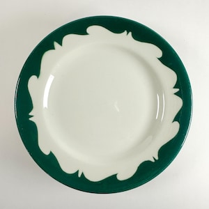 May include: A white ceramic plate with a dark green rim and a white scalloped design. The plate has a simple, elegant design, suitable for everyday use or special occasions. The plate is round.