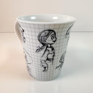 May include: White ceramic mug with black and white cartoon character sketches. The mug has a handle and a grid pattern. The sketches include a side profile of a girl with a ponytail.
