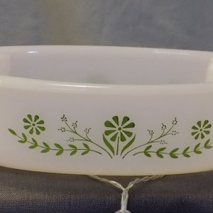 May include: White oval baking dish with a green floral design. The design features a repeating pattern of small green flowers and leaves.