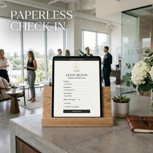 Puede incluir: Una tableta digital que muestra un formulario de registro de invitados, apoyada en un soporte de madera. La pantalla muestra campos para nombre, correo electrónico y número de teléfono. Las palabras "PAPERLESS CHECK-IN" están en la parte superior. El fondo muestra un entorno de oficina.