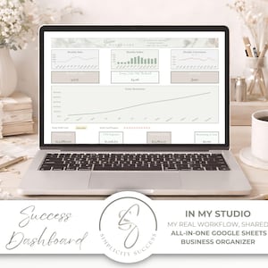 Pode incluir: Um laptop exibindo um painel de negócios com gráficos. A tela mostra análise de dados com as palavras "Success Dashboard" e "In My Studio" na parte inferior. Uma caneca de café, flores e artigos de papelaria são dispostos ao redor do laptop.