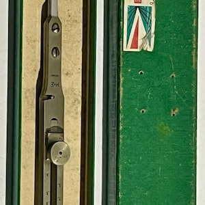 May include: A silver-toned metal proportional divider tool with a sliding adjustment knob, marked K+E, resting in a green box. The box label reads MARK I PROPORTIONAL DIVIDERS 8 IN. 55 1872, featuring a red K+E logo and a blue and red graphic design.
