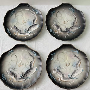 May include: A set of four scalloped-edge plates featuring a central dragon motif. The plates have a gradient design transitioning from a dark charcoal gray rim to a light cream center, accented with light blue cloud-like swirls and gold details.