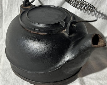 Tetera vintage de hierro fundido con mango de acero inoxidable, tapa giratoria, base y hervidor para fogata.
