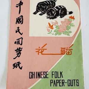 May include: A vintage paper-cut art booklet with a pink and green cover. The cover features black cat illustrations, floral designs, and Chinese characters. The text "CHINESE FOLK PAPER-CUTS" is printed in black.