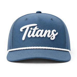 May include: A blue baseball cap featuring the word Titans in raised white script lettering across the front panel. The cap includes a white braided rope detail running horizontally across the base of the crown, just above the curved brim.