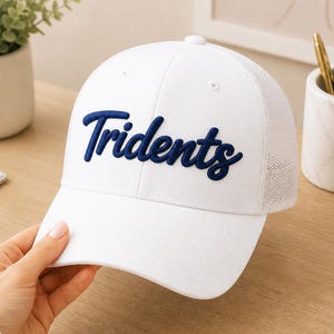 May include: White baseball cap with the word "Tridents" embroidered in navy blue script across the front. The cap has a mesh back and a curved brim. A stylish accessory for casual wear.
