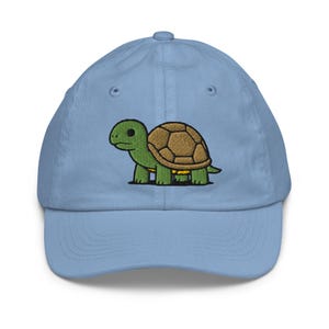 May include: A light blue baseball cap with an embroidered cartoon turtle. The turtle has a green head and legs, a brown shell, and is on the front of the cap. The cap has a curved peak and an adjustable strap at the back.