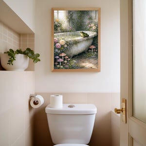 May include: A framed art print depicts a whimsical scene of a vintage bathtub surrounded by flowers, mushrooms, and a frog. The artwork is in a bathroom setting, above a white toilet and next to a shelf with a potted plant. The frame is a light brown color.