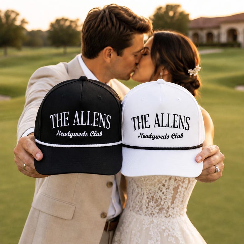 Op de afbeelding: Een zwarte honkbalpet met witte tekst THE ALLENS Newlyweds Club en een wit koord, naast een witte honkbalpet met zwarte tekst THE ALLENS Newlyweds Club en een zwart koord, beide voorzien van een gestructureerde kroon.