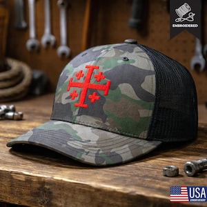 Peut inclure: Casquette de baseball camouflage avec une croix de Jérusalem rouge brodée sur le devant. La casquette a un dos en filet noir et une visière incurvée. Le mot "EMBROIDERED" est imprimé sur la casquette.