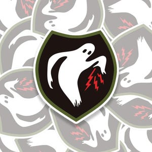 May include: A collection of stickers featuring a white ghost design with a red lightning bolt graphic on a black shield. The shield has a green border. The stickers are on a white background.