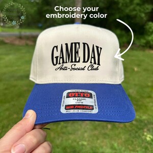 Op de afbeelding: Een tweekleurige baseballpet met een cr&egrave;mekleurige kroon en een koningsblauwe klep. De pet heeft de tekst "GAME DAY Anti-Social Club" in zwart. De pet heeft een "MID PROFILE" label.