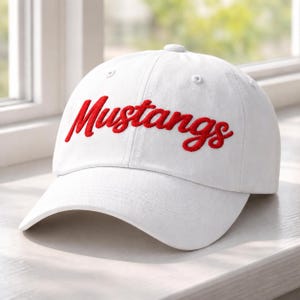 May include: White baseball cap with the word "Mustangs" embroidered in red script across the front. The cap has a curved brim and a button on top. A classic, casual accessory.