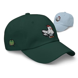 May include: Two baseball caps, one dark green and one light blue, are displayed. The dark green cap features an embroidered pixelated chicken on the front and a small green creature on the side. The light blue cap has a chicken design.