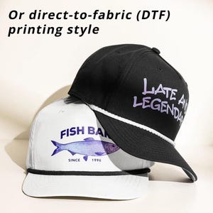 K&ouml;nnte beinhalten: Eine wei&szlig;e Baseballkappe mit blauem Fischmotiv und dem Text "FISH BAN SINCE 1996" sowie eine schwarze Baseballkappe mit dem violetten Text "LATE AND LEGENDARY", mit wei&szlig;er Kordel am Schirm und dem Text "Or direct-to-fabric (DTF) printing style".