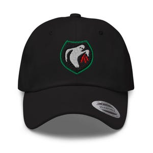 May include: Black baseball cap with an embroidered patch showing a white ghost-like figure holding a red object, set against a green and black shield. The cap has a curved peak and an adjustable strap.