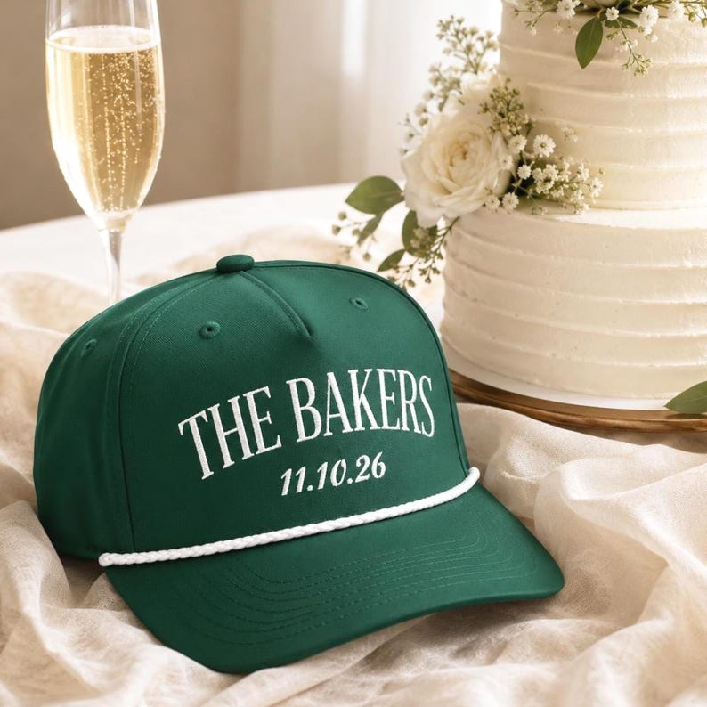 Op de afbeelding: Een donkergroene honkbalpet met een wit koorddetail over de klep. De voorkant van de pet toont de witte tekst THE BAKERS boven de datum 11.10.26 in een strak, vet lettertype. De pet is gemaakt met een gestructureerde kroon en ventilatiegaatjes.