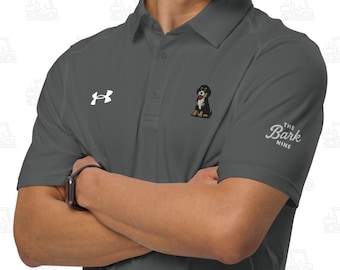 May include: A dark gray short-sleeved polo shirt featuring a white Under Armour logo on the right chest, a small graphic of a Bernese Mountain Dog in the center, and the text The Bark Nine embroidered in white on the left sleeve.