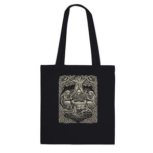 Puede incluir: Bolso tote negro con una ilustración detallada. La obra de arte representa tres figuras vestidas con túnicas alrededor de un pozo bajo un gran árbol. El diseño es en tonos grises y blancos, con intrincados bordes de nudos celtas.