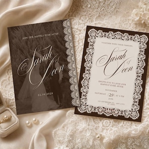 May include: Two rectangular wedding invitation cards with dark brown borders and white lace-style patterns. One card features a sepia-toned photograph of a couple, while the other displays text details. A ring in a beige velvet box sits nearby.