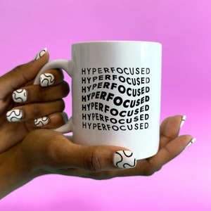 May include: White ceramic mug with a black design that says "HYPERFOCUSED" repeated in a spiral pattern.