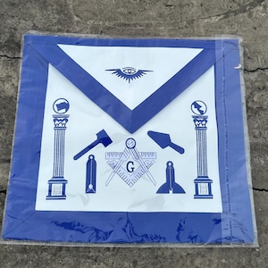 Puede incluir: Un delantal masónico azul con bordados blancos. El delantal presenta una escuadra y un compás, un nivel, una paleta, dos pilares y un ojo que todo lo ve.