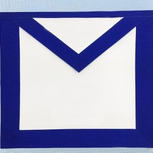 Peut inclure: Un tablier blanc avec une bordure bleue et un motif en forme de V bleu en haut. Le tablier est rectangulaire avec une bordure bleue texturée. Le fond est un tissu bleu clair.