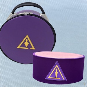 Puede incluir: Un estuche de viaje redondo morado con un asa negra y un sombrero morado a juego. Ambos artículos presentan un emblema triangular dorado con una figura en su interior. El sombrero tiene un interior rosa.