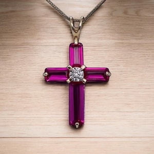 Puede incluir: Un collar con un colgante de oro en forma de cruz rosa con un pequeño diamante en el centro.