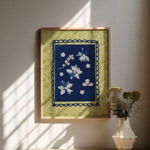 May include: A framed print with a blue background and white floral designs. The frame is light wood and the background of the print is a light green.