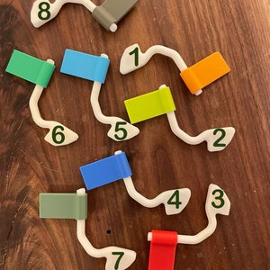 May include: A white plastic track with eight numbered flags in different colors. The flags are green, blue, orange, yellow, blue, green, red, and gray. The track is numbered 1 through 8.