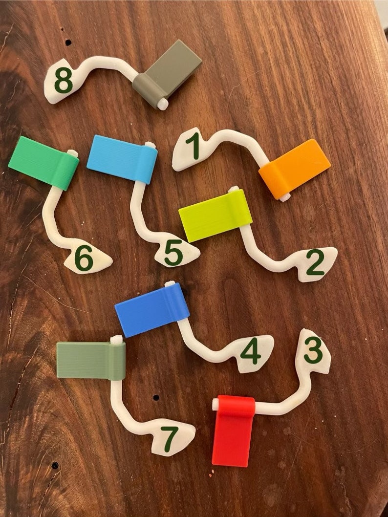 May include: A white plastic track with eight numbered flags in different colors. The flags are green, blue, orange, yellow, blue, green, red, and gray. The track is numbered 1 through 8.