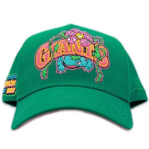 May include: Green baseball cap with a pink and yellow embroidered logo that says "Giants" with a cartoon green, blue, and pink creature in the middle of the logo.