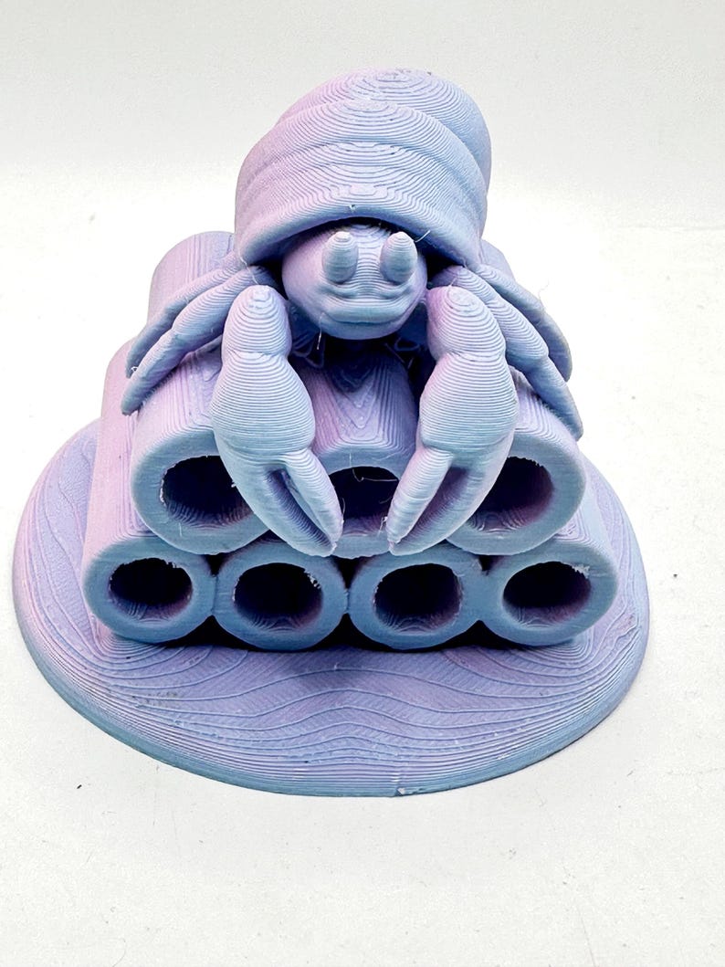 Puede incluir: Escultura impresa en 3D de un cangrejo con caparaz&oacute;n, pinzas y m&uacute;ltiples estructuras tubulares. La escultura es en tonos morados y azules, con un aspecto texturizado y en capas. El cangrejo se asienta sobre una base circular.