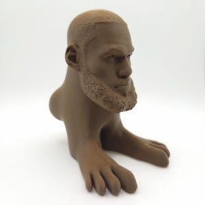 May include: A brown sculpture of a human head with a beard and short hair, connected to a body with feet. The sculpture is a solid colour and appears to be 3D-printed. The head has detailed facial features.