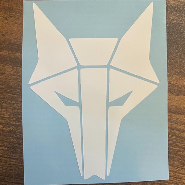 May include: White geometric wolf head sticker on a light blue background. The design features sharp angles and a symmetrical layout, creating a modern and stylized look. The sticker is likely for application on various surfaces.