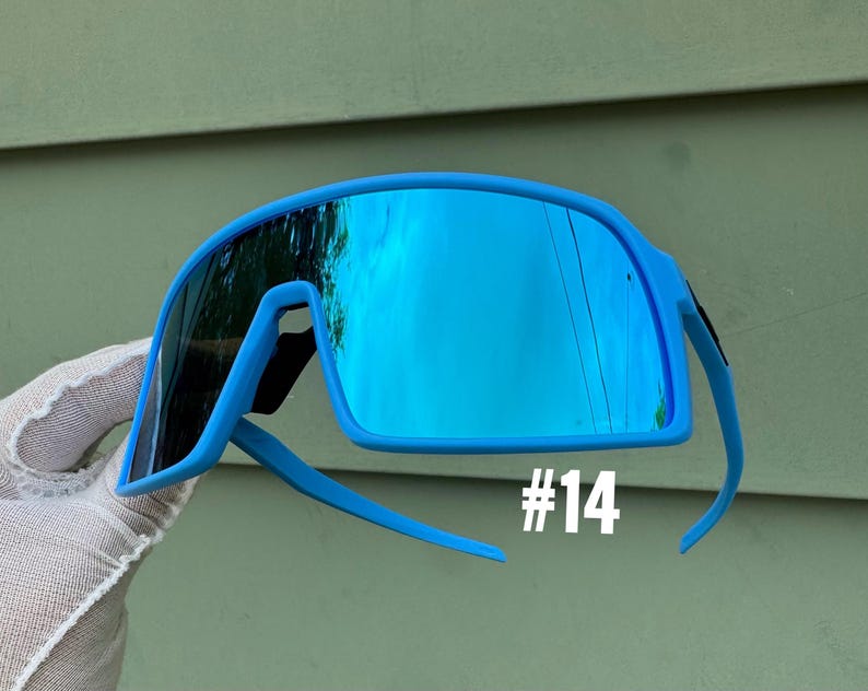 May include: Bright blue sport sunglasses with mirrored lenses. The sunglasses have a wraparound design and a bold, modern aesthetic. The number "#14" is printed in white on the lower right side of the frame. The lenses reflect the surrounding environment.
