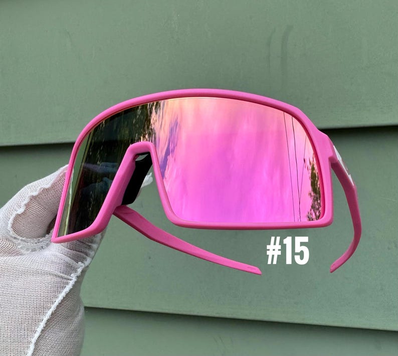 May include: Bright pink sunglasses with mirrored lenses. The sunglasses have a bold, wraparound design with a thick frame and arms. The number "#15" is printed in white on the lower right side of the frame.