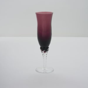 May include: A single, elegant champagne flute with a deep purple hue that fades to black at the base. The stem is clear, twisted glass, and the foot is a simple, round base. The glass is designed for special occasions.