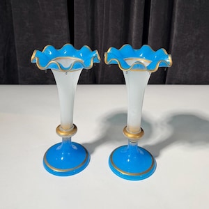 May include: A pair of glass vases featuring a white central stem that transitions into a vibrant blue base and a ruffled blue rim. Each vase is accented with gold painted trim along the base, the central ring, and the scalloped top edge.