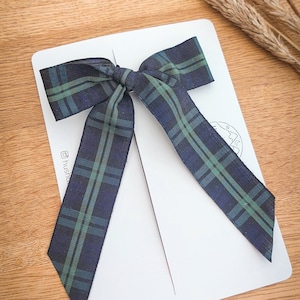 May include: A white card with a green and blue plaid bow tied on top. The card has the text "@hush.co" printed on it.