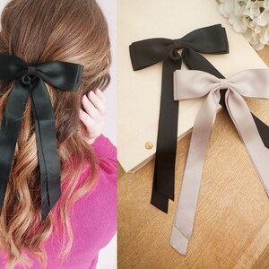 May include: Two hair bows with long tails. One bow is black satin and the other is a light gray satin.