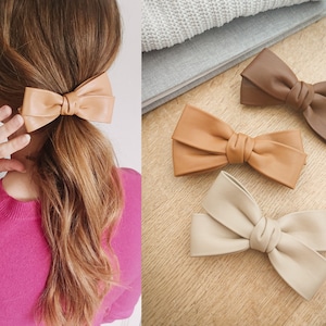 May include: Three faux leather hair bows in different shades of brown. The bows are tied in a simple knot and have a slightly textured finish.