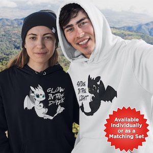 Può includere: Una felpa con cappuccio nera con una grafica di drago bianco e il testo Glow in the Dark e una felpa con cappuccio bianca con una grafica di drago nero e il testo Shine in the Light. Entrambe hanno maniche lunghe, cappucci e tasche frontali.
