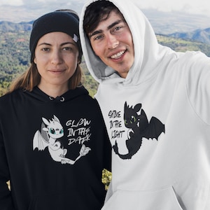 Könnte beinhalten: Zwei Personen tragen schwarze und weiße Hoodies mit einem Drachen-Motiv und dem Text "Glow in the dark" und "Shine in the light".