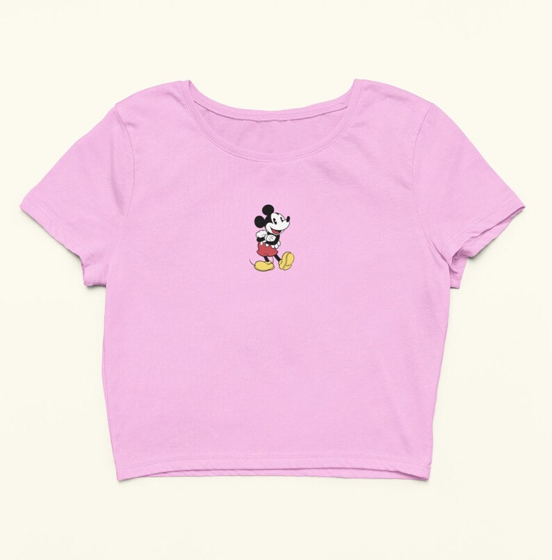 Peut inclure: Un t-shirt rose p&acirc;le &agrave; manches courtes et &agrave; ourlet court, avec une image de Mickey Mouse au centre.