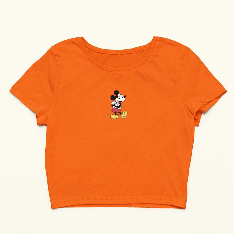 Peut inclure: T-shirt orange &agrave; manches courtes et &agrave; ourlet court avec une petite image brod&eacute;e de Mickey Mouse au centre.